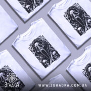 Футболка хорор скрім, біла футболка на манекені, з принтом чорного кольору, що зображує маску з фільму жахів, на фоні світло-сірого кольору, деталі принта включають черепи та елементи, що нагадують про жахи.