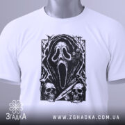 Футболка хорор скрім, складена біла футболка з принтом чорного кольору, що зображує маску з фільму жахів, на фоні світло-сірого кольору, з етикеткою зеленого кольору, що звисає з коміра.