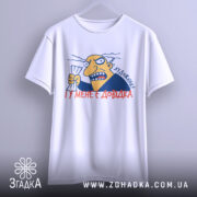 Футболка художник маю довідку. Біла футболка, підвішена на вішалці, з принтом на грудях. Принт зображає персонажа з жовтим обличчям, який тримає аркуш паперу, з написом 'Я художник! І у мене є довідка'. Фон світло-сірий, футболка має округлий виріз.