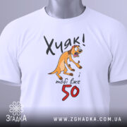 Футболка Хуяк тобі 50, біла, складена на поверхні, з видимим етикеткою, фон світло-сірий, принт з жовтим собакою, що виглядає здивованою, текст чорний і червоний.