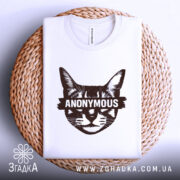 Футболка кіт анонімус білого кольору, складена на плетеній основі, фон світло-сірий, принт зображає кота з написом 'ANONYMOUS' у коричневому кольорі, видно етикетку з написом.