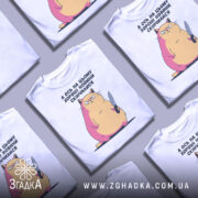 Футболка кіт погані новини, біла, зображена на манекені, фон градієнтний сірий, принт зображує кота з ножем, з рожевими і жовтими відтінками.