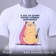 Футболка кіт погані новини, біла, складена на поверхні, фон світлий, принт з котом з ножем, з рожевими і жовтими відтінками, з етикеткою на рукаві.