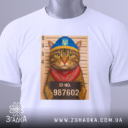 Футболка кіт у розшуку, біла, складена на столі, фон світло-сірий, принт з котом у блакитній шапці та червоному бандану, на фоні ліній для зросту з написом ID NO. 987602, з етикеткою на шнурку.