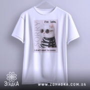 Футболка кіт у стилі білого кольору, підвішена на вішалці, фон світло-сірий, принт з котом у сонцезахисних окулярах та смугастому светрі, текст на футболці говорить 'I'm late, I didn't want to come.'