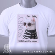 Футболка кіт у стилі білого кольору, зображена на столі, фон світло-сірий, принт з котом у сонцезахисних окулярах та смугастому светрі, текст на футболці говорить 'I'm late, I didn't want to come.', на футболці є етикетка з зеленим шнурком.