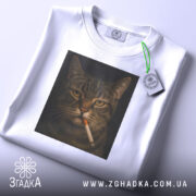 Футболка кіт з цигаркою, біла, складена на поверхні, фон світло-сірий, принт з котом, що курить, з етикеткою на шнурку.