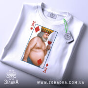 Футболка король черви, біла, складена на поверхні, фон світло-сірий, принт з ілюстрацією короля червів, який тримає келих з вином, з короною на голові, з червоними ромбами, на футболці є етикетка.