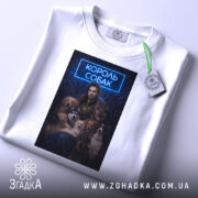 Футболка король собак, біла, складена на поверхні, фон світлий, принт з зображенням чоловіка з собаками, текст "КОРОЛЬ СОБАК" у неоновому стилі, на футболці є етикетка.