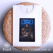 Футболка король собак, біла, складена на плетеній кошику, фон світлий, принт з зображенням чоловіка з собаками, текст "КОРОЛЬ СОБАК" у неоновому стилі.