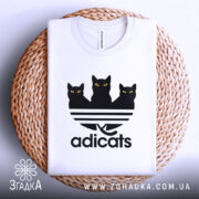 Футболка котячий стиль adicats, біла, складена на плетеній основі, з видимим принтом трьох чорних котів з жовтими очима на смугастому фоні, фон білий.