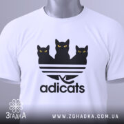 Футболка котячий стиль adicats, біла, складена на поверхні, з видимим етикеткою, принт з трьома чорними котами з жовтими очима на смугастому фоні, з легким відблиском.