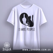 Футболка коти ненавиджу людей, біла, підвішена на вішалці, фон світло-сірий, принт чорного кольору з силуетом кота та жестом руки, видно округлі краї рукавів.