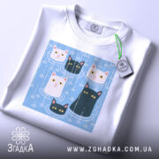 Футболка коти під дощем, біла, зображена зверху, фон світло-сірий, принт з п'ятьма котами на блакитному фоні, з етикеткою на комірці.