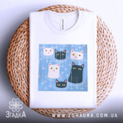 Футболка коти під дощем, біла, зображена зверху на плетеній кошику, фон світло-сірий, принт з п'ятьма котами на блакитному фоні, добре видно деталі принта.