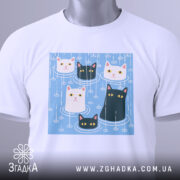 Футболка коти під дощем, біла, зображена зверху, фон світло-сірий, принт з п'ятьма котами на блакитному фоні, з етикеткою на комірці.