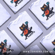 Футболка котик бариста, біла, зображена на манекені, фон світло-сірий, принт з котиком у фартуху, що тримає чашки з кавою, текст 'MR. BARISTA' під малюнком.