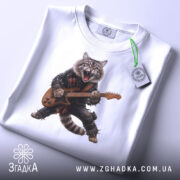 Футболка котик рокер гітарист, біла, складена на поверхні, фон світло-сірий, принт з котом у рокерському стилі, з гітарою, прикріплена етикетка з логотипом.