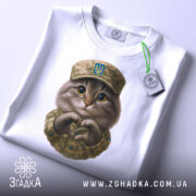 Футболка котик захисник, біла футболка на столі, фон світло-сірий, принт з котиком у військовій формі, на футболці є етикетка.