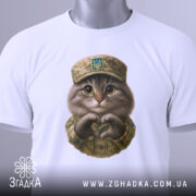 Футболка котик захисник, біла футболка на столі, фон світло-сірий, принт з котиком у військовій формі, на футболці є етикетка.