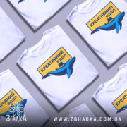 Футболка креативний відділ, біла, зображена на манекені, фон світло-сірий, принт з синім дельфіном у капелюсі та жовтим написом "КРЕАТИВНИЙ ВІДДІЛ".