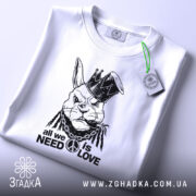 Футболка кролик панк, біла, зображена зверху, на фоні світлого градієнта. Принт зображає кролика в короні з дредами, з написом 'all we need is love' під ним, з етикеткою, що звисає.