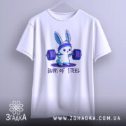 Футболка кролик сила, біла футболка, підвішена на вішалці, з принтом кролика, що піднімає важкі штанги, на фоні світло-сірого кольору, принт яскравий і кольоровий.