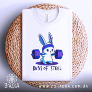 Футболка кролик сила, біла футболка, складена на плетеній кошику, з принтом кролика, що піднімає штанги, на фоні світло-сірого кольору, принт чіткий і яскравий.