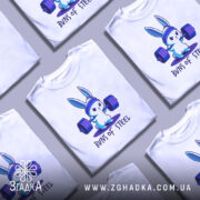 Футболка кролик сила, біла футболка на манекені, з принтом кролика, що піднімає важкі штанги, на фоні світло-сірого кольору, принт виконаний у відтінках синього та фіолетового.