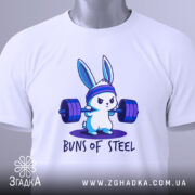 Футболка кролик сила, біла футболка, складена на столі, з принтом кролика, що піднімає штанги, на фоні світло-сірого кольору, з етикеткою зеленого кольору.