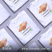 Футболка круасанний гумор Prashant, білого кольору, зображена з правого ракурсу на манекені, фон світло-сірий, принт з зображенням круасана та текстом 'CROISSANT' з червоним хрестиком і 'PRASHANT' з зеленим галочкою.