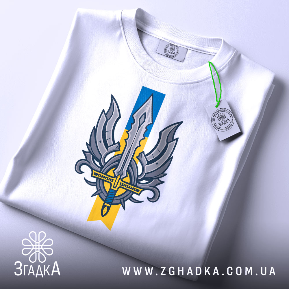 Футболка крила меч свободи, біла, складена на столі, фон світло-сірий, принт з мечем та крилами, на етикетці зелена стрічка.