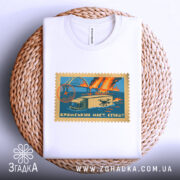 Футболка Кримський міст, біла, складена на плетеній основі, фон білий, принт у вигляді поштової марки з малюнком мосту, вантажівки та дронів, кольори принта: блакитний, оранжевий, жовтий.