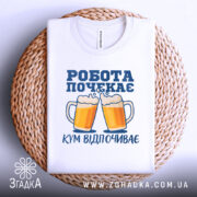 Футболка кум відпочиває, біла, складена на плетеній основі, фон світлий, принт з двома пивними кухлями та написом 'РОБОТА ПОЧЕКАЄ' у синьому кольорі.