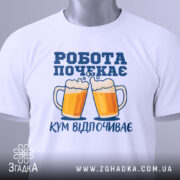 Футболка кум відпочиває, біла, складена на поверхні, фон світлий, принт з двома пивними кухлями та написом 'РОБОТА ПОЧЕКАЄ' у синьому кольорі, з зеленим ярликом.