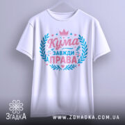 Футболка кума завжди права. Біла футболка з коротким рукавом, підвішена на вішалці, зображена спереду. На фоні світло-сірий градієнт. Принт у рожевих та блакитних кольорах, з написом 'Кума завжди права' та декоративними елементами.