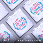 Футболка кума завжди права. Біла футболка з коротким рукавом, зображена з правого ракурсу на манекені. На фоні світло-сірий градієнт. Принт виконаний у рожевих та блакитних тонах, з написом 'Кума завжди права' та декоративними елементами у вигляді листя та сердець.