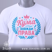 Футболка кума завжди права. Складена біла футболка, зображена зверху під кутом. На фоні світло-сірий градієнт. Принт у рожевих та блакитних кольорах, з написом 'Кума завжди права' та елементами декору, такими як корона та ваги.