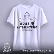 Футболка квітів не потрібно. Біла футболка з коротким рукавом, підвішена на вішалці. На футболці чорний принт з усміхненим персонажем і текстом "А ось і Я! Квітів не потрібно!". Фон світло-сірий, що створює контраст з футболкою.