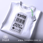 Футболка Київ білого кольору, складена на поверхні, фон світлий, принт у вигляді штрих-коду з написами 'Київ', 'RESET SYSTEM', 'CITY OF CHESTNUTS' та 'SCAN FOR FREEDOM', на комірці видна етикетка.