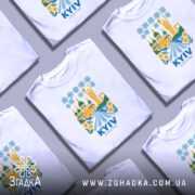 Футболка Київ білого кольору, зображена на манекені, з принтом, що містить архітектурні елементи Києва, включаючи статую матері-героїні, квіти та річку, фон світло-сірий.