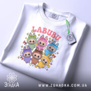 Футболка labubu білого кольору, складена на поверхні, з видимим етикеткою, фон світло-сірий, принт з кольоровими персонажами та написом 'LABUBU' у верхній частині.