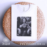 Футболка леді у центрі уваги, біла, зображена зверху на плетеній основі, на фоні світлого градієнта, принт з чорно-білим зображенням жінки з сигаретою, руки оточують її.