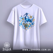 Футболка лелека з квітами, біла, підвішена на вішалці, фон світло-сірий, принт з лелекою та квітами в блакитних і жовтих тонах.