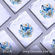 Футболка лелека з квітами, біла, зображена з правого ракурсу, фон світло-сірий, принт з лелекою та квітами в блакитних і жовтих тонах.