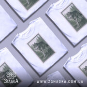 Футболка лісовий вовк, біла, зображена на манекені, фон світло-сірий, принт з лісовим вовком у зелених тонах на фоні лісу, оформлений у рамку.