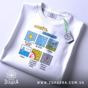 Футболка любіть Україну, білого кольору, складена на поверхні, фон світлий, принт з кольоровими малюнками та текстом, на комірці видна етикетка з логотипом.