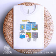 Футболка любіть Україну, білого кольору, складена на плетеній основі, фон натуральний, принт з кольоровими малюнками та текстом, видно комірку футболки.