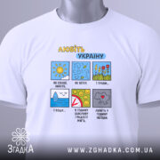 Футболка любіть Україну, білого кольору, складена на поверхні, фон світлий, принт з кольоровими малюнками та текстом, на комірці видна етикетка з логотипом.