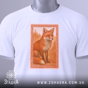Футболка лисиця білого кольору, складена на столі, з верхнього ракурсу. Принт зображає лисицю в оранжевих тонах, оформлений в рамку, поряд з етикеткою на зеленому шнурку.